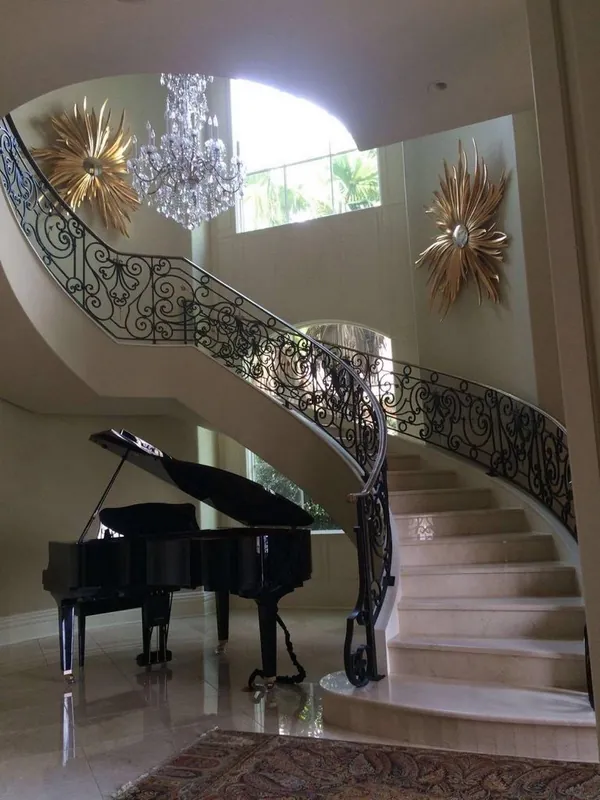 A curved staircase with an ornamental iron railing and a piano below.