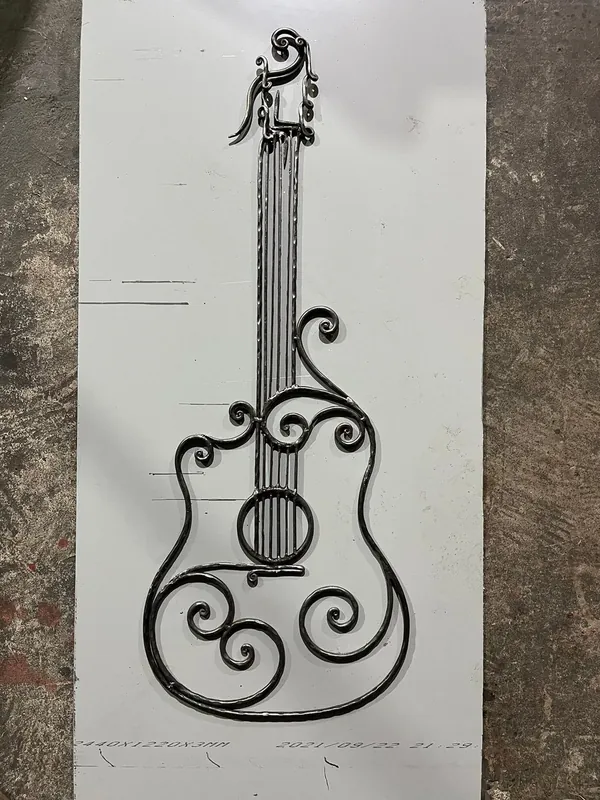 A guitar-shaped metal object with strings and scrolls, lying on a sheet of metal.